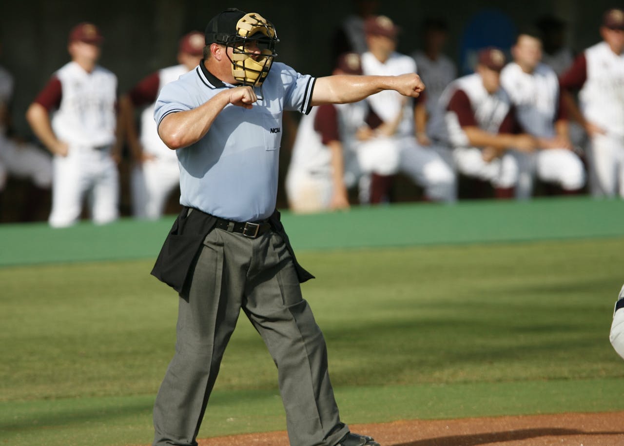 hero-img Umpire in action on baseball field with team players in the background.